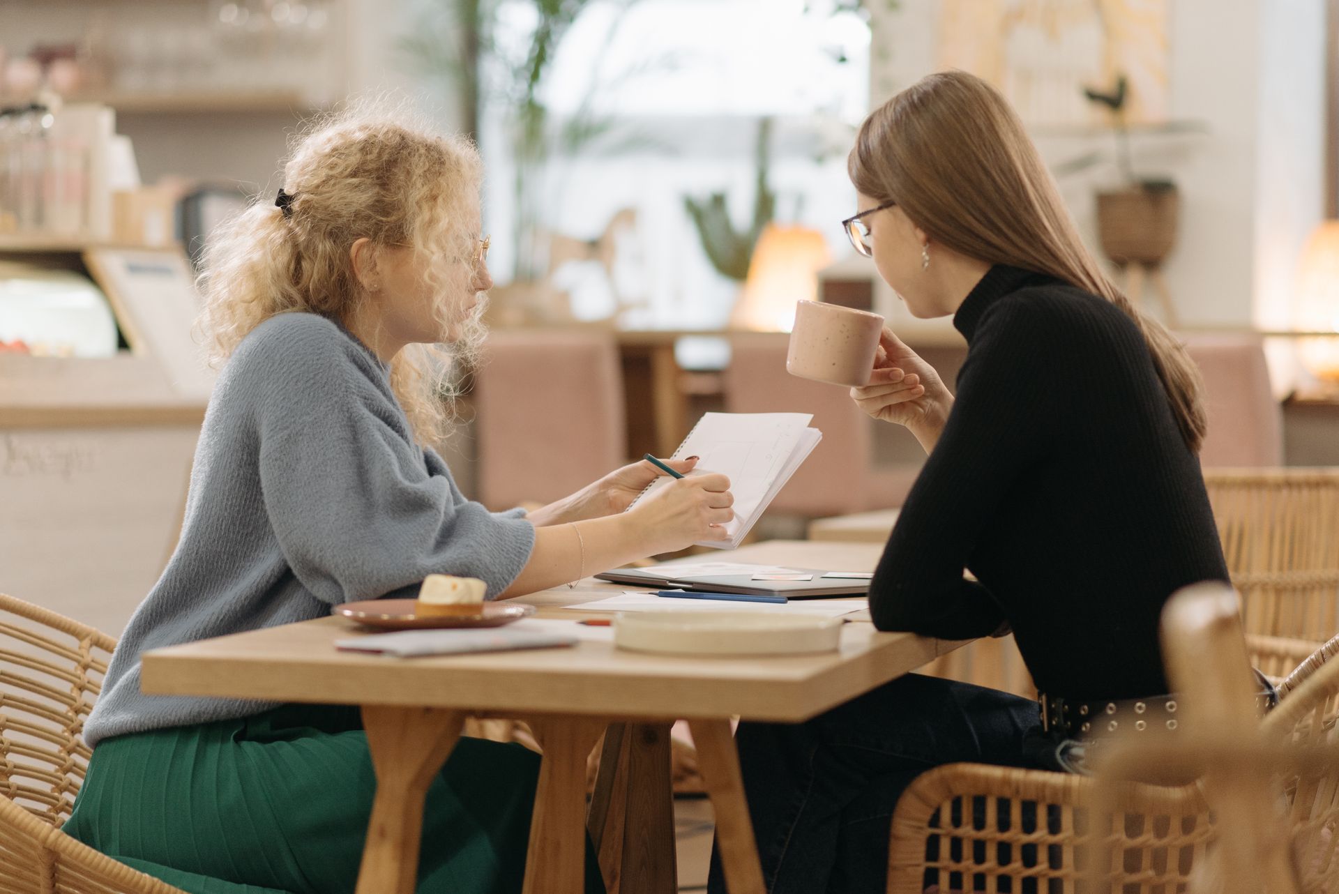 Two women discussing ideas over coffee in a cozy cafe, focused and engaged in conversation.