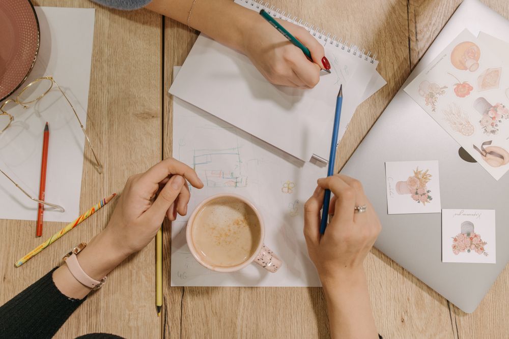 Overhead view of hands sketching plans on a wooden desk. Photo by Pavel Danilyuk on Pexels