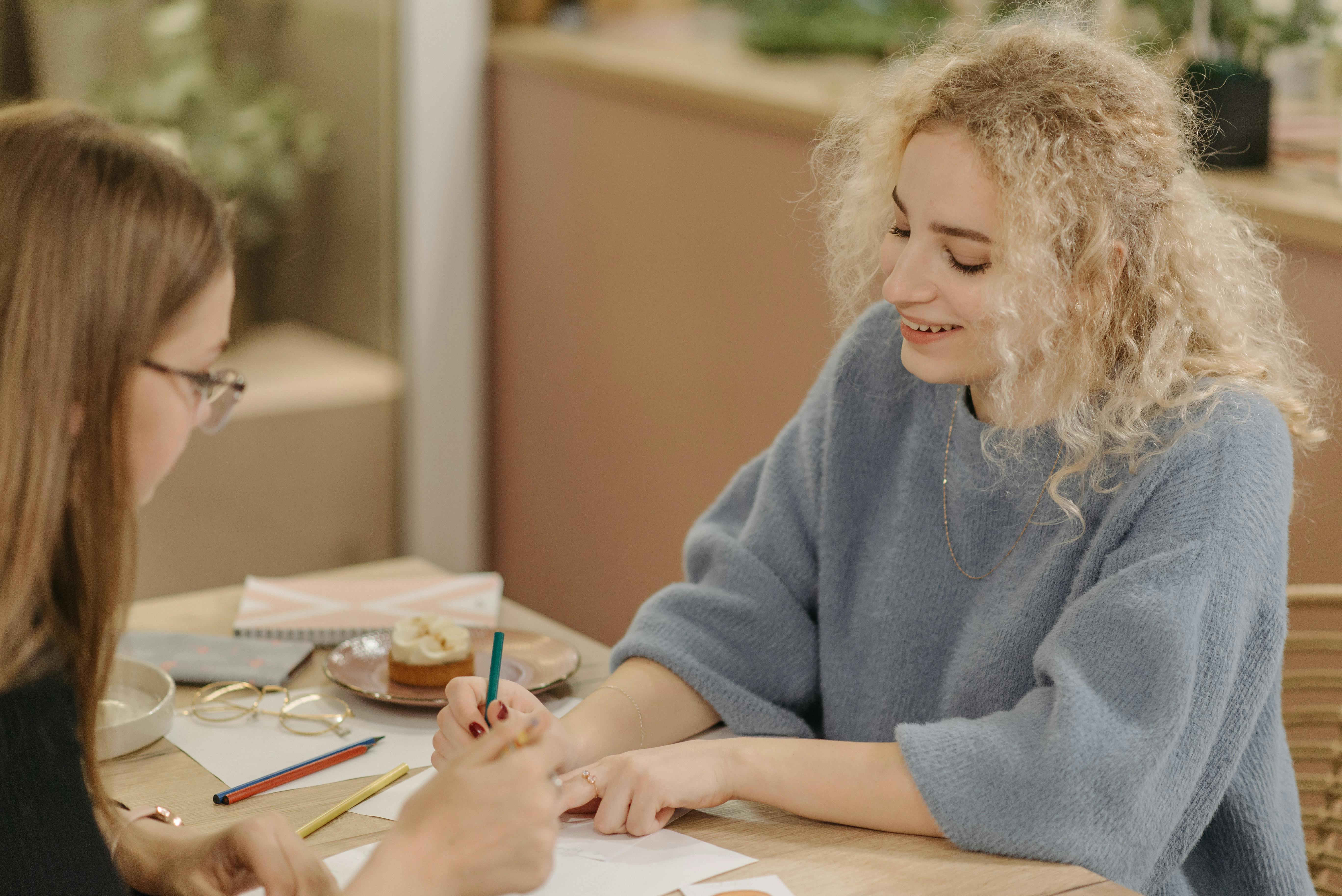 Two women discussing a creative project at a desk with pencils and paper.