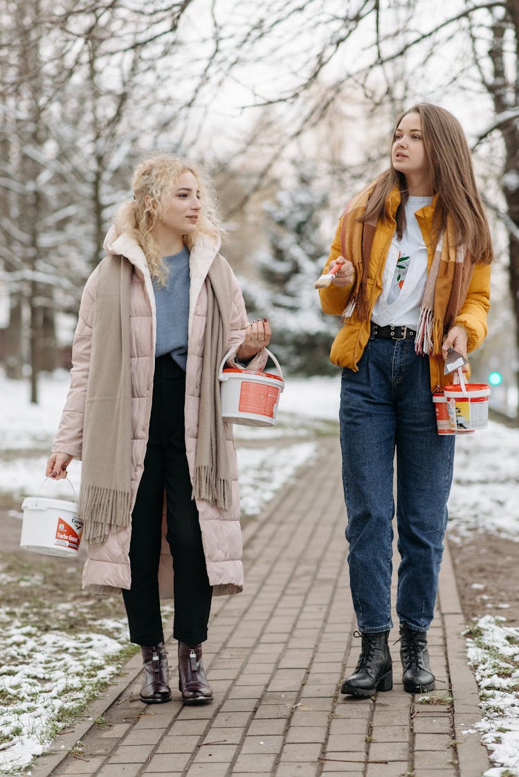 Women In Winter Jackets Walking On Pathway Holding Paint In Buckets