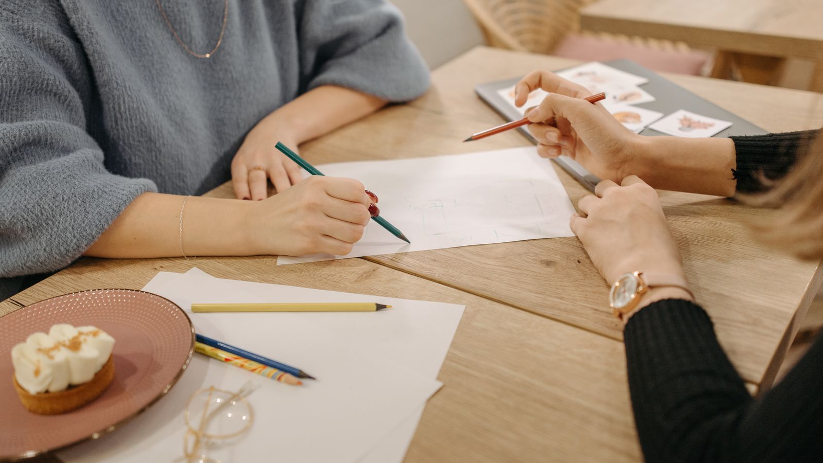 Two people drawing with coloured pencils at a wooden table