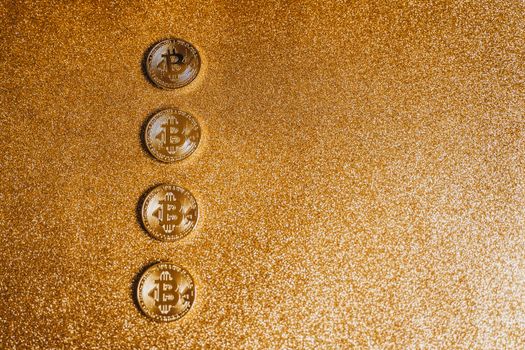 Four Bitcoin coins arranged on a shimmering gold glitter background with ample copyspace.