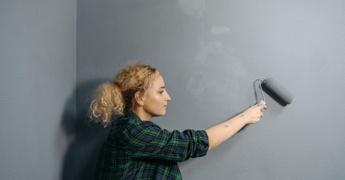 Painter rolling fresh gray paint onto an interior wall during a home repaint