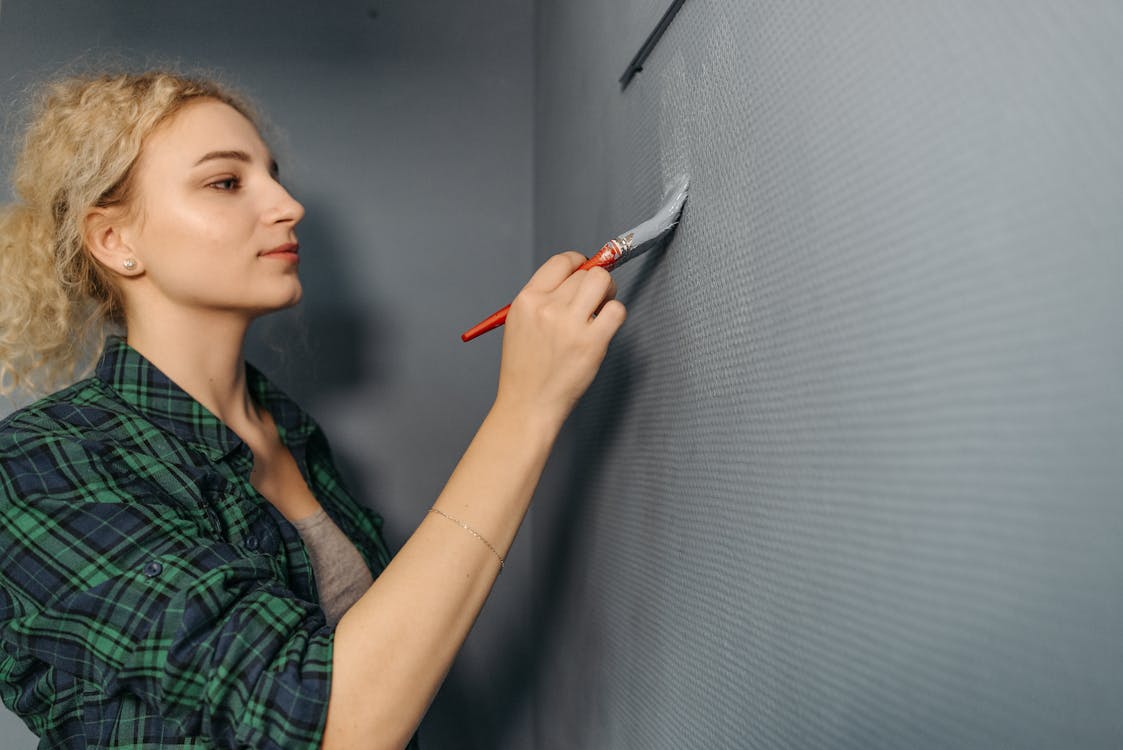 A Woman in a Plaid Shirt Painting a Wall