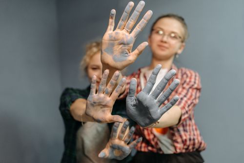 Free Close-up of hands with paint, showing creativity and joy. Two women smiling in the background. Stock Photo
