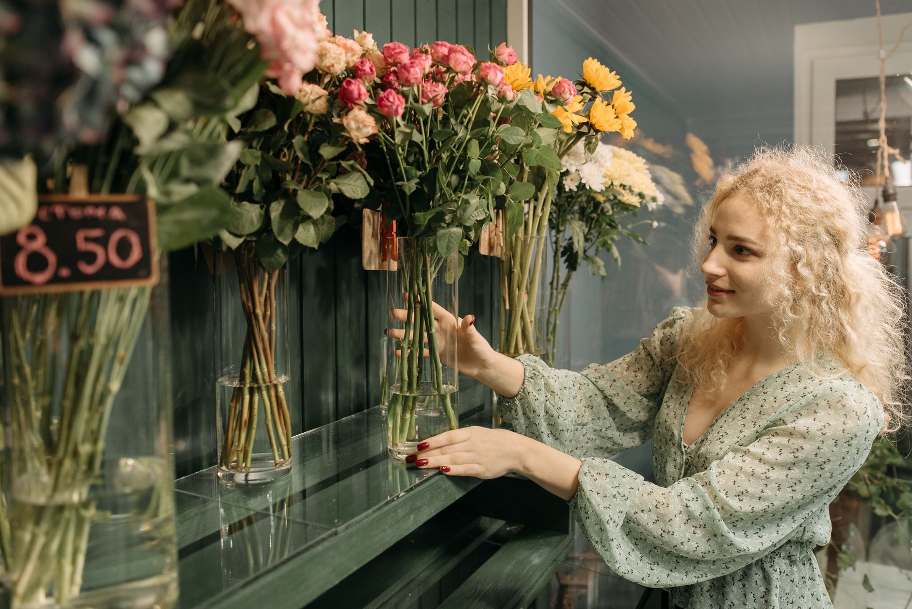 A cheerful woman arranging vibrant flowers in a cozy floral shop indoor setting.