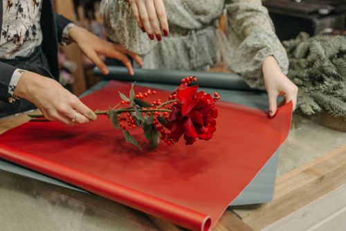 Free Close-up of hands wrapping a red rose in vibrant red wrapping paper, symbolizing love and gifts. Stock Photo
