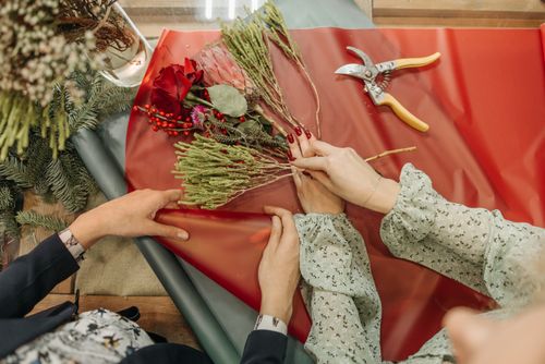 Free Two women collaborate on creating festive bouquets using red flowers and greenery. Stock Photo