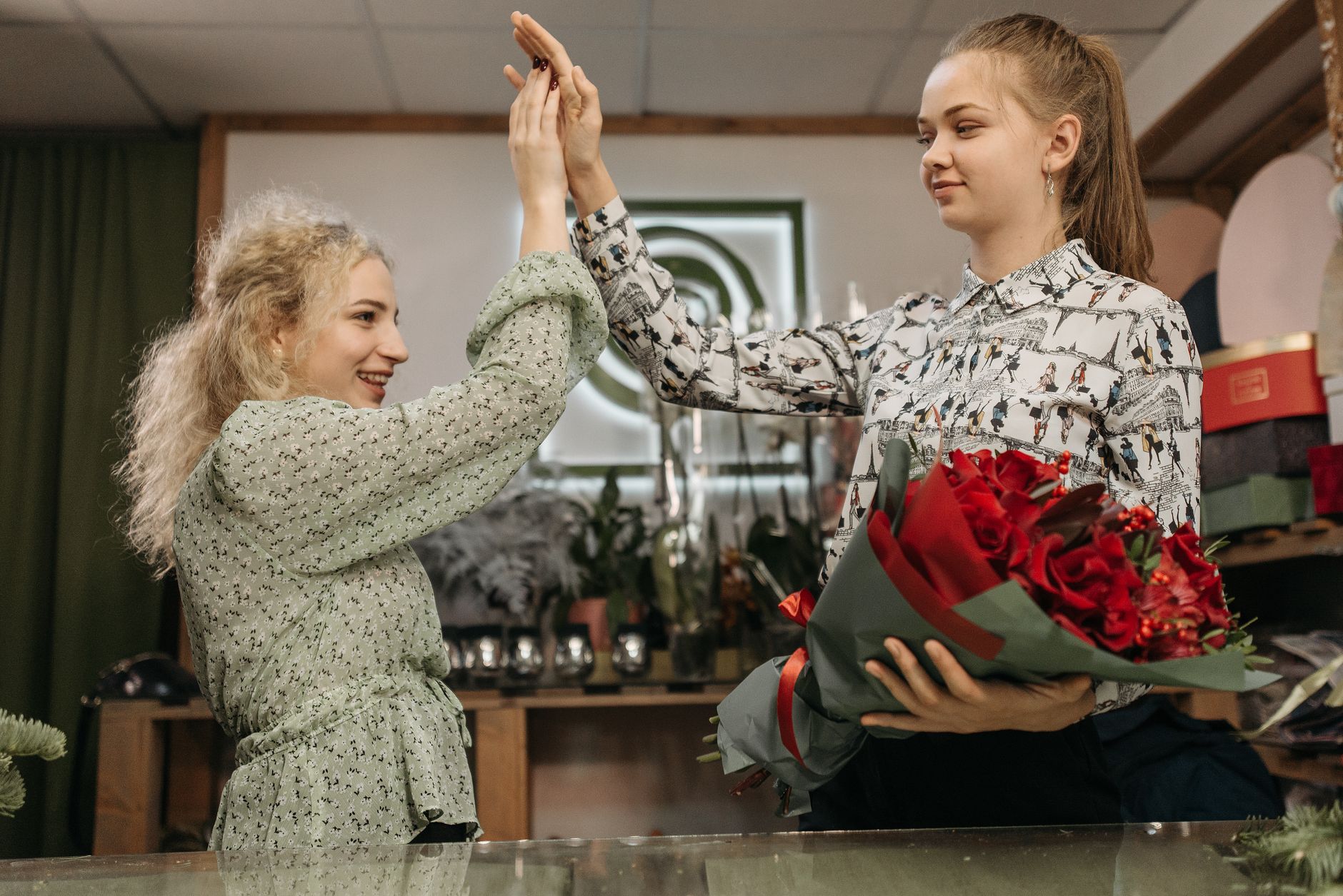 Two women enjoying a moment with red flowers and a high five indoors.