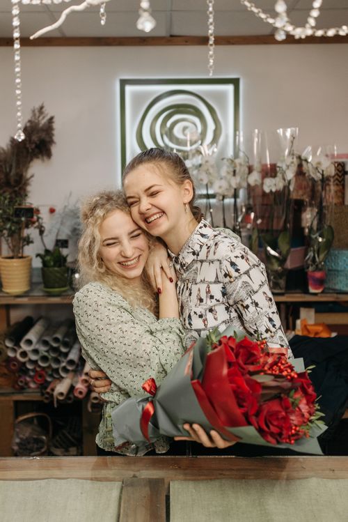 Free Two women share a joyful embrace in a flower shop, holding a vibrant bouquet. Stock Photo
