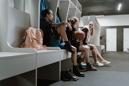 Three women sitting in a basketball locker room, showcasing team spirit and diversity.