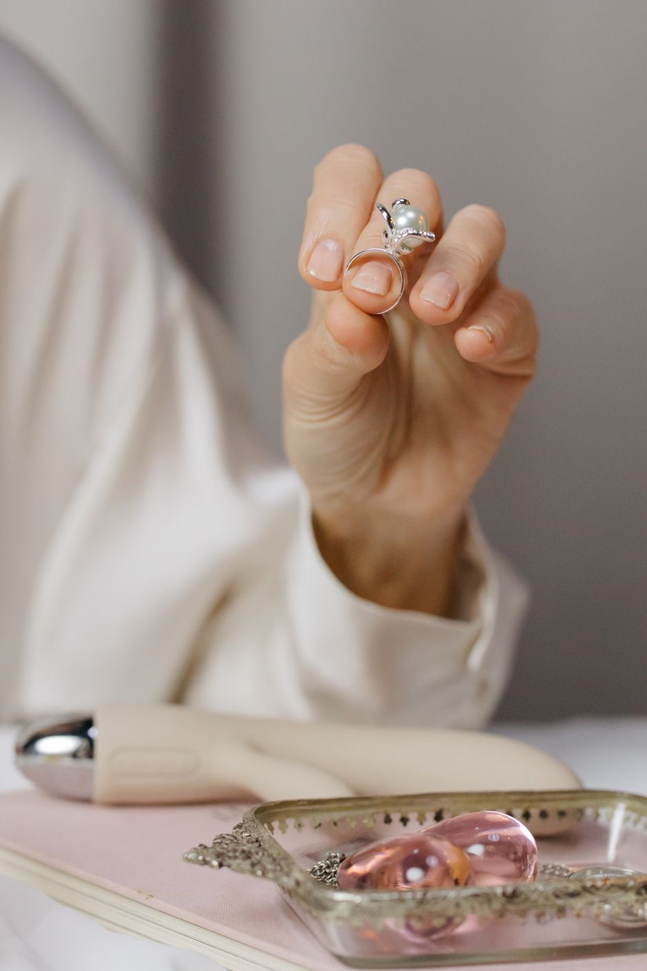 A woman holding a pearl ring above a jewelry tray