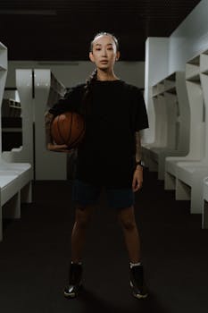 Confident young athlete posing with basketball in stylish locker room setting.