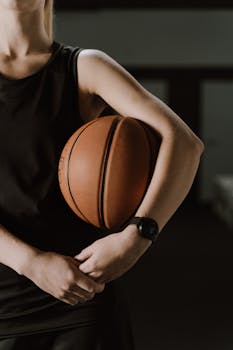 Close-up of a woman in sportswear holding a basketball indoors.