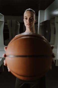 A woman holds a basketball, standing in a locker room, ready for the game.
