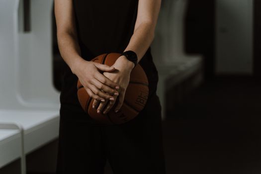 A close-up shot of a basketball player holding a ball in a dimly lit indoor space.