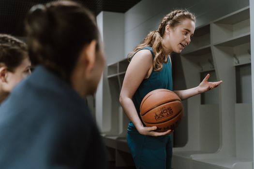 A young female basketball player explains strategies to teammates in a locker room.