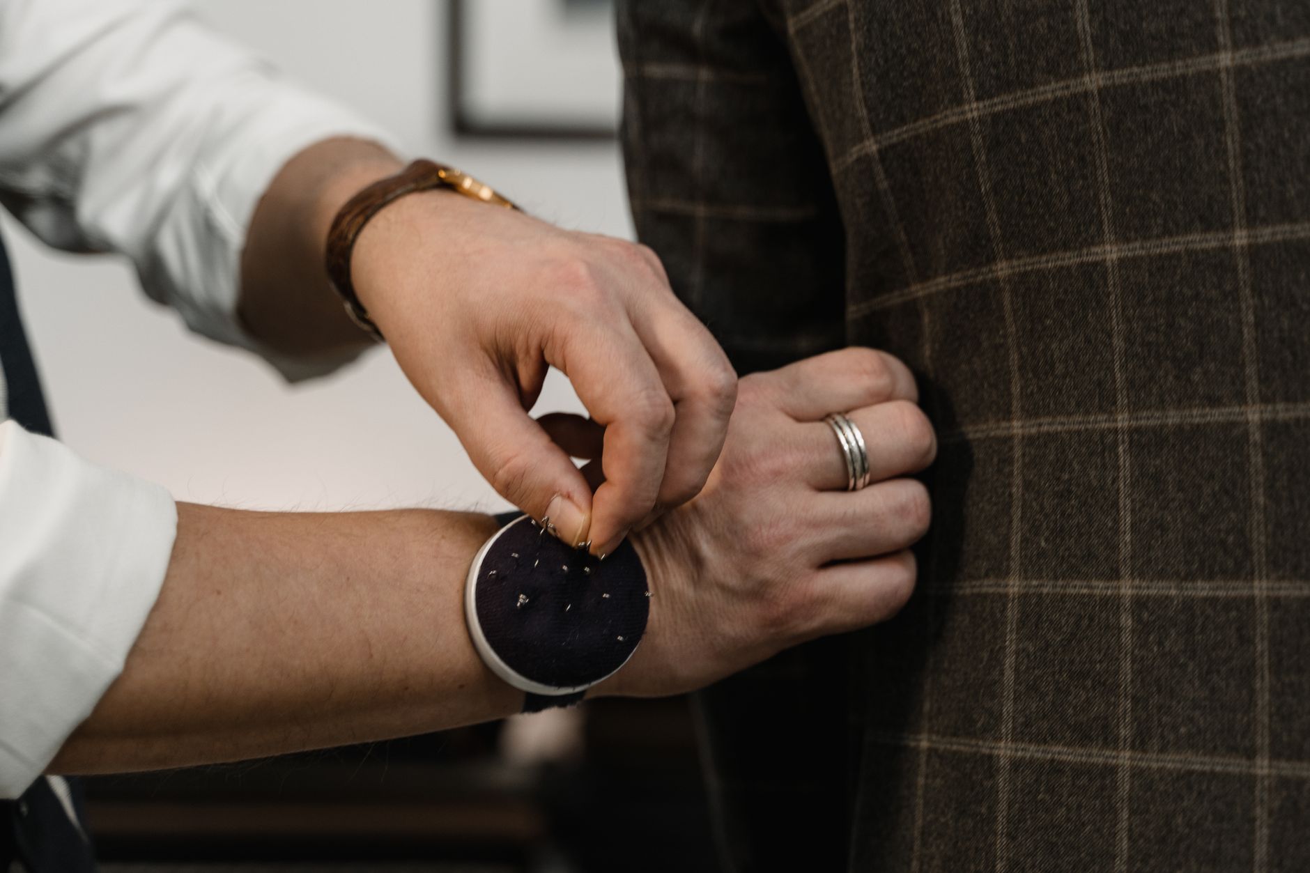 Close-up of a tailor adjusting a checkered suit jacket during a fitting session.
