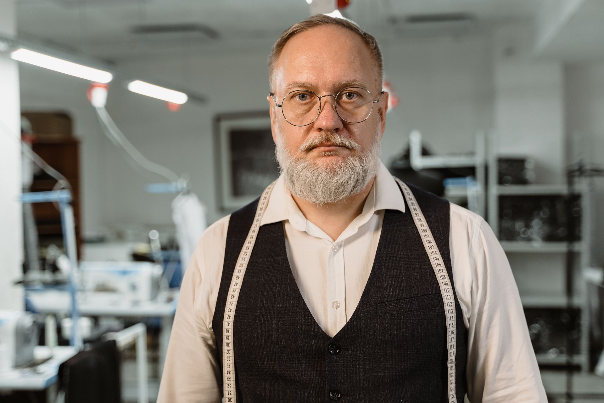 Elderly male fashion designer wearing glasses and a suit in an indoor studio setting.