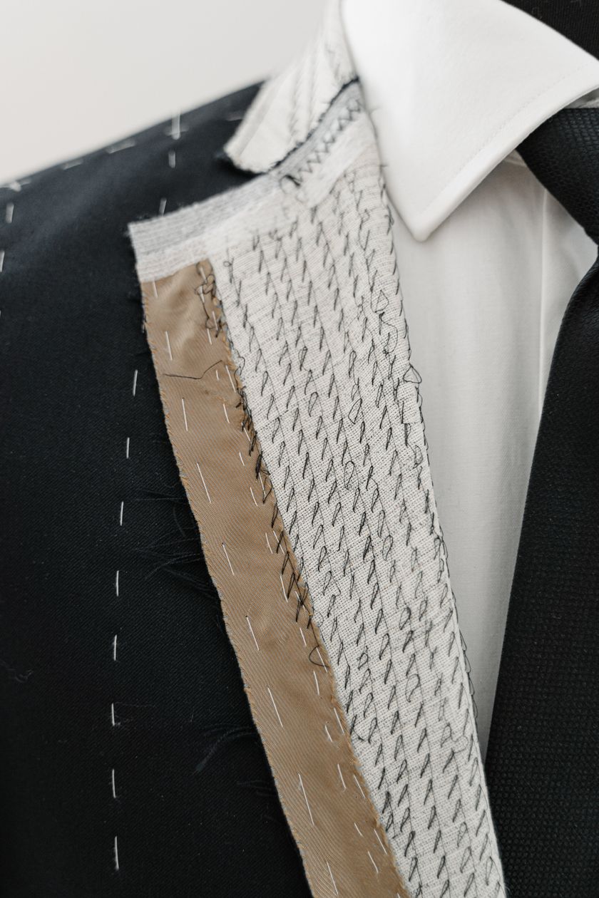 Close-up of an unfinished jacket front: a pale canvas held to the panel with rows of pad stitching and basting thread.