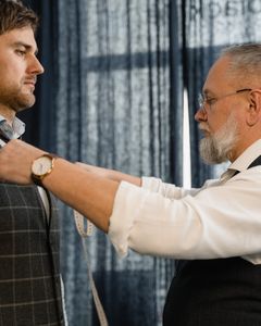 Professional tailor measuring a client for a custom suit in a workshop setting.