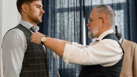 Professional tailor measuring a client for a custom suit in a workshop setting.