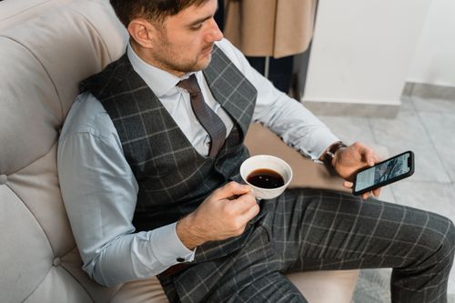 Free Businessman in plaid suit enjoying coffee and browsing on phone indoors. Stock Photo