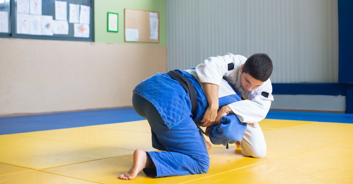 Two men practicing judo techniques on a dojo mat indoors.