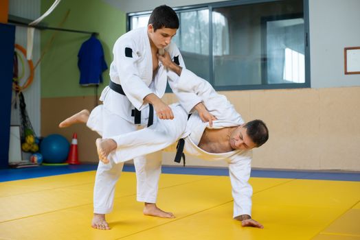 Dynamic action shot of two men practicing judo, showcasing technique and movement in an indoor gym setting.