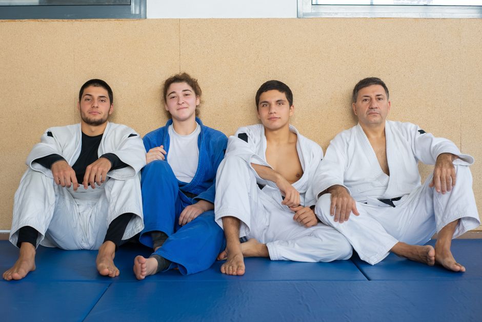 道着を着た4人の柔道家が一緒に座り、チームワークと武道の disciplineを示しています。