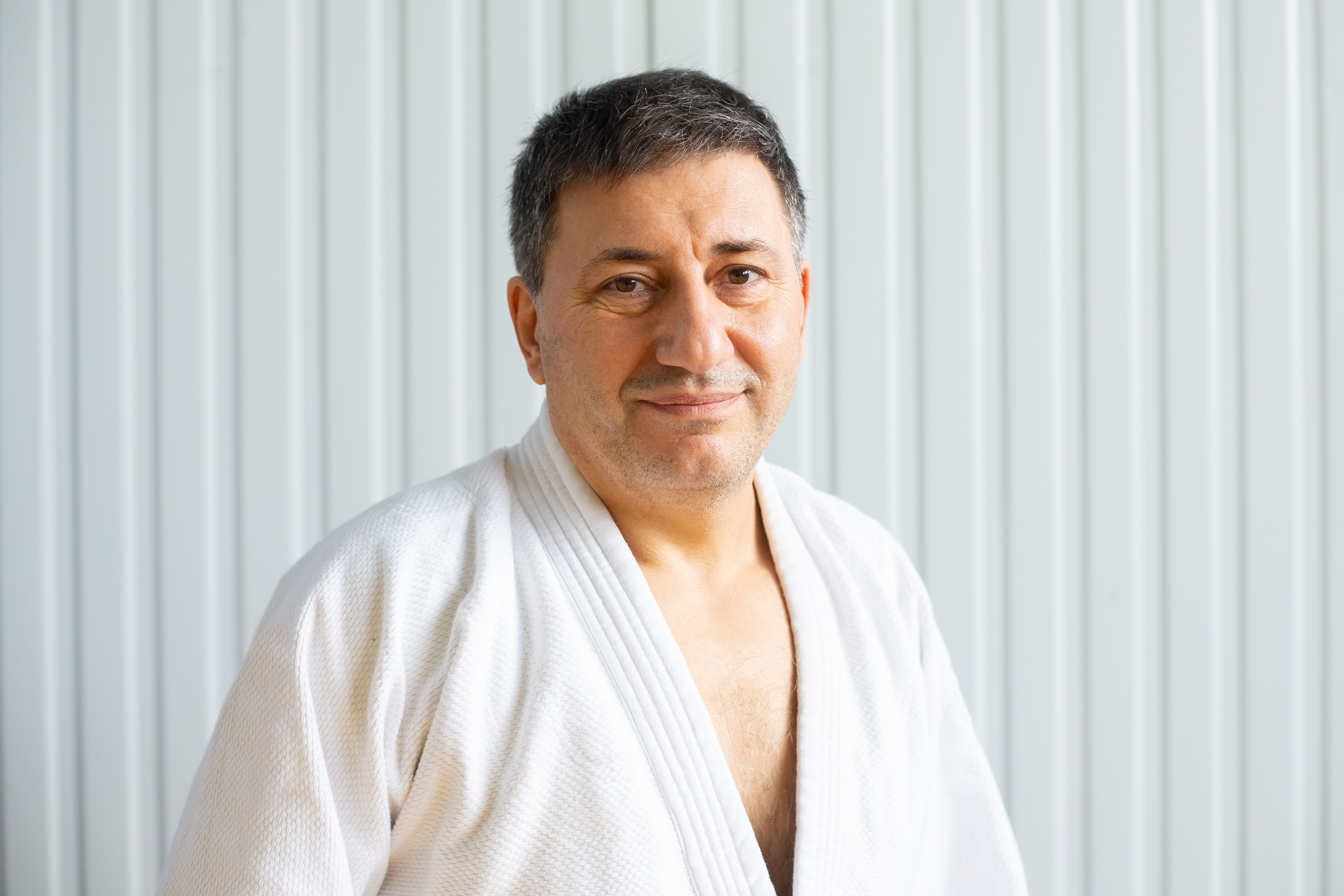 A confident middle-aged man wearing a martial arts gi, smiling in an indoor setting.