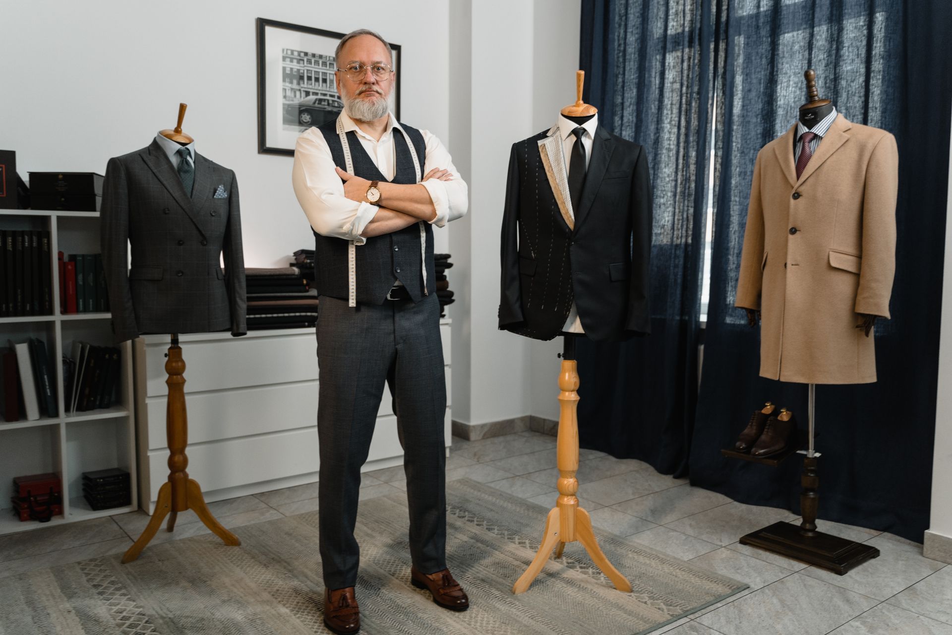 Tailor posed with mannequins displaying elegant designer suits in a studio setting.