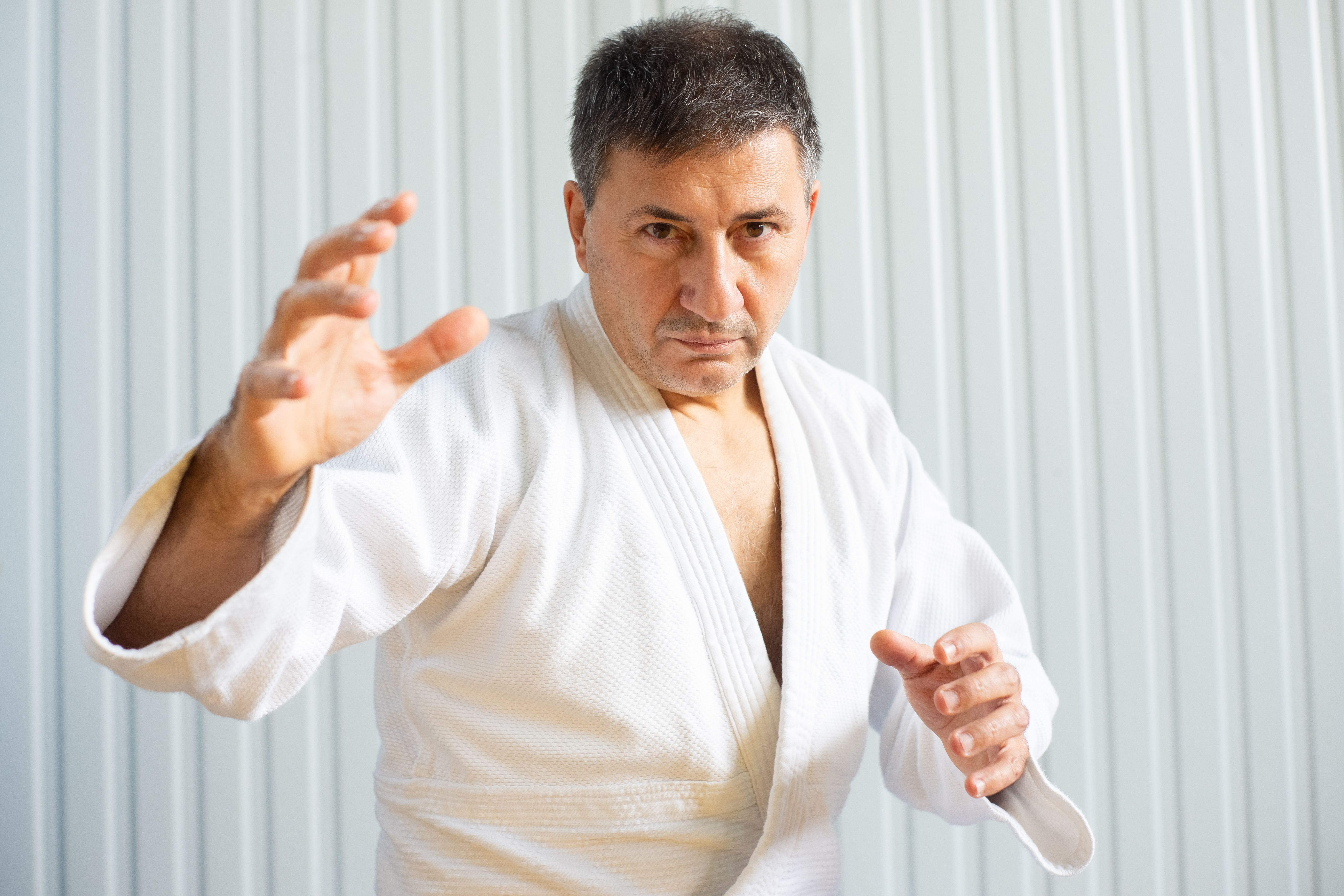 A man practicing martial arts indoors, wearing a judo uniform and striking a focused pose.