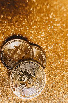 Three shiny Bitcoin coins on a glittery gold surface symbolizing cryptocurrency and digital finance.