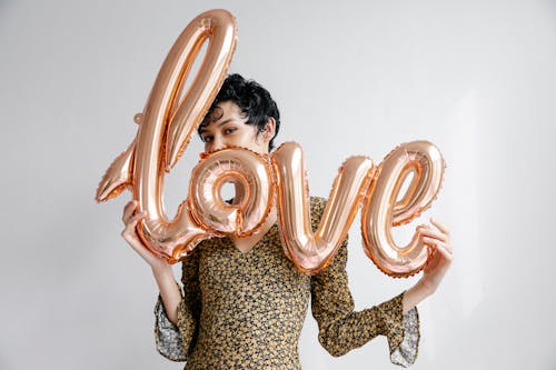 Cheerful smiling female demonstrating sparkling festive balloon with word love and looking at camera on white background