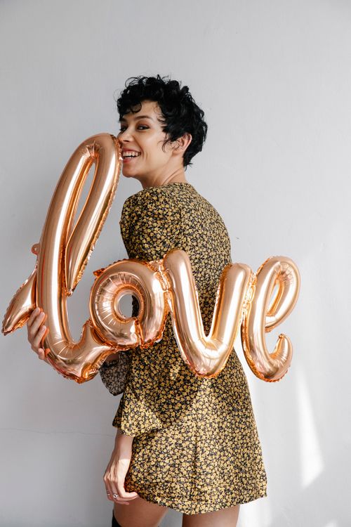 Free Positive young female in festive elegant dress demonstrating shiny balloon while smiling and looking at camera on white background Stock Photo