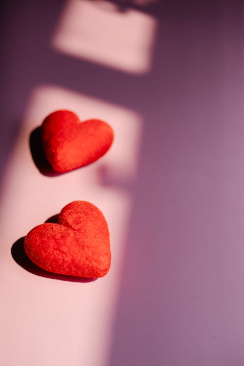 From above of red decorative hearts placed on pink background lightened by sunshine