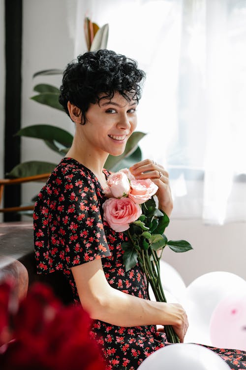 Free Side view positive female sitting bunch of flowers while sitting on sofa among balloons and looking at camera Stock Photo