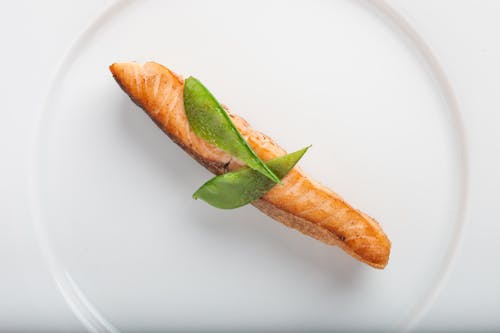 Pescado Cocido Con Dos Hojas Verdes En Plato Redondo De Cerámica Blanca