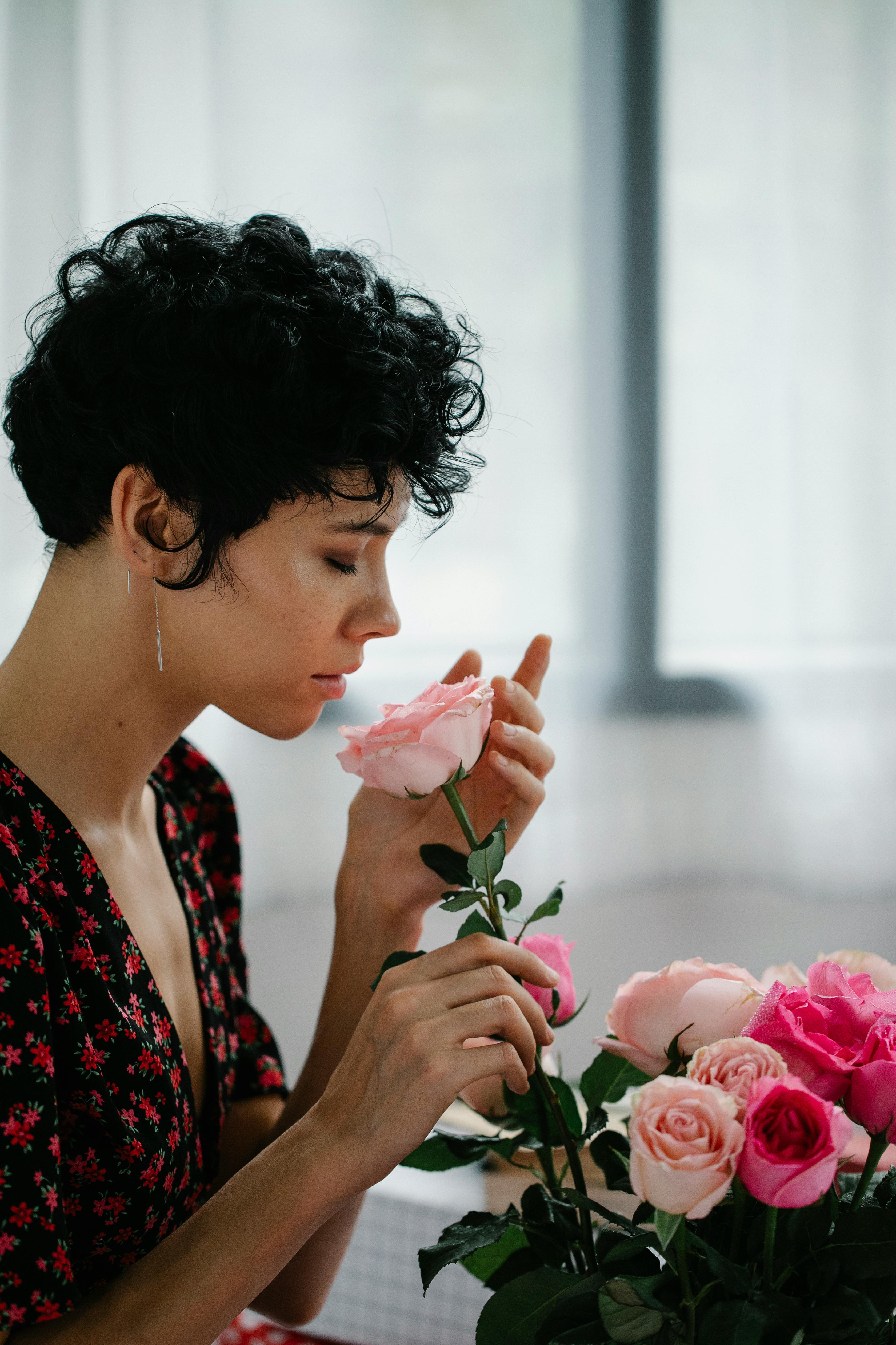 a woman with curly short hair smelling a pink rose
