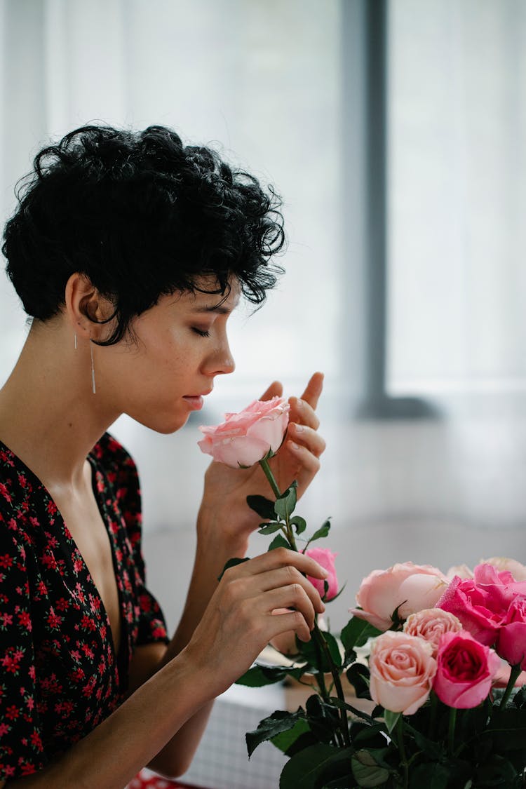 A Woman With Curly Short Hair Smelling A Pink Rose