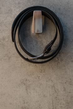 Elegant black leather belt with silver buckle, neatly rolled on a concrete background for a stylish look.