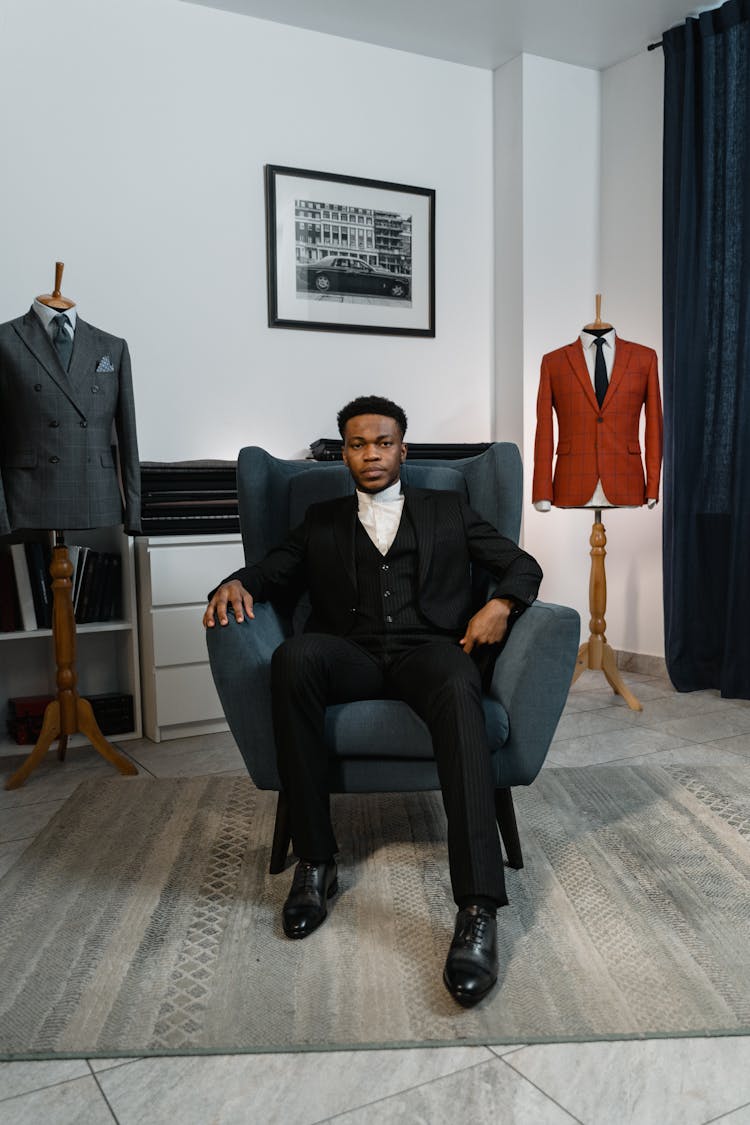 A Man In Black Suit Sitting On A Chair