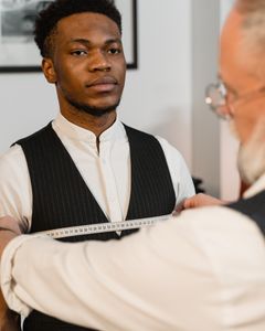 A professional tailor measuring a young man's chest for a perfectly fitted suit.