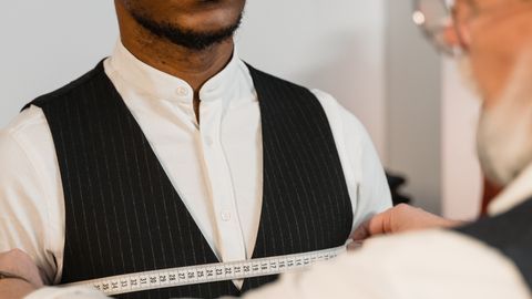 A professional tailor measuring a young man's chest for a perfectly fitted suit.