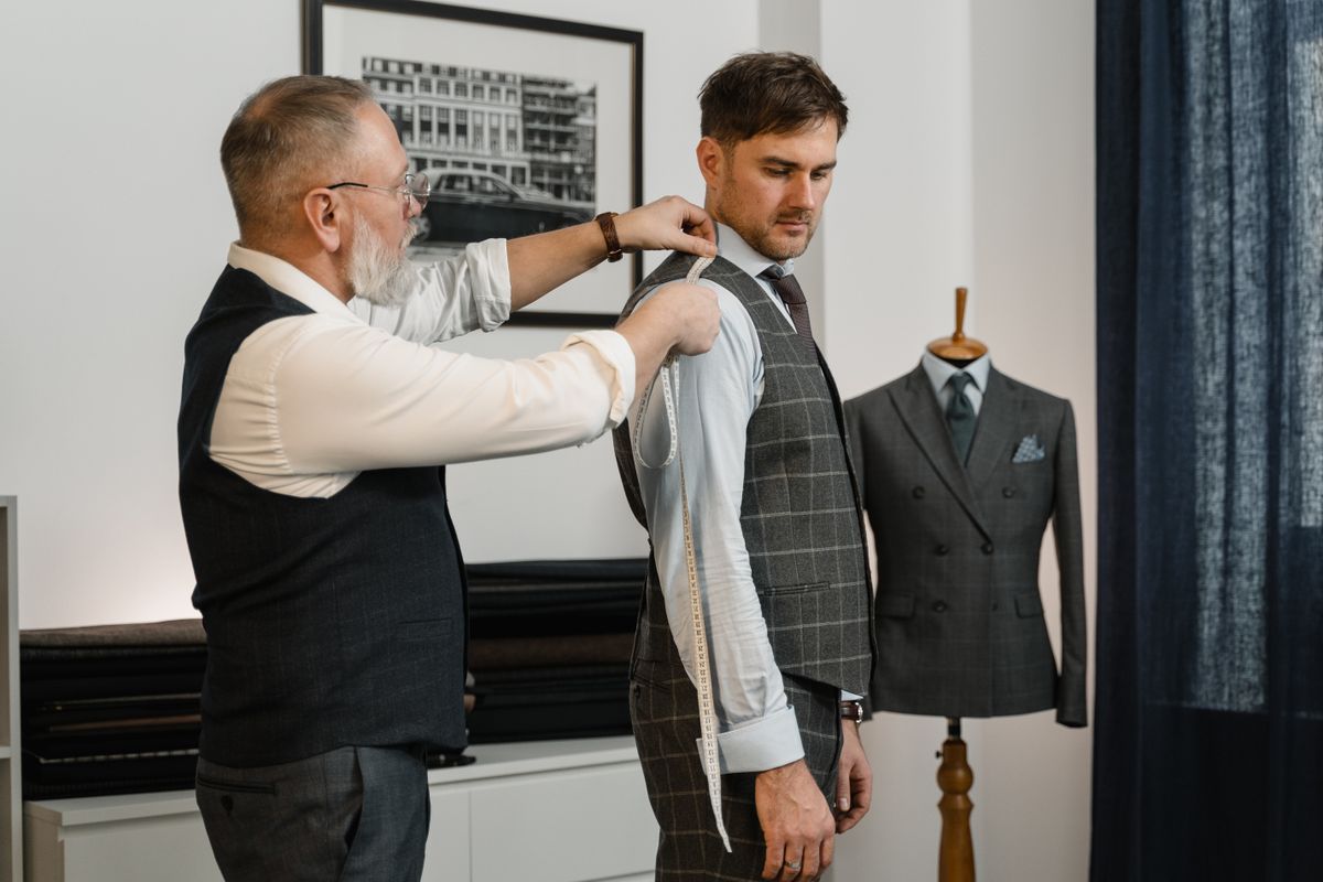 A tailor fitting a jacket on a client, marking the shoulder