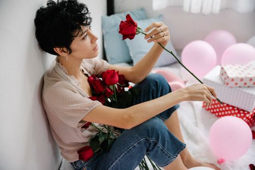 Free Side view from above of calm female with red rose sitting on floor with colorful balloons and gift boxes while celebrating holiday Stock Photo