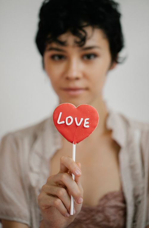 Free Crop young ethnic lady with dark curly hair demonstrating heart shaped lollipop with Love inscription during Saint Valentines Day celebration Stock Photo