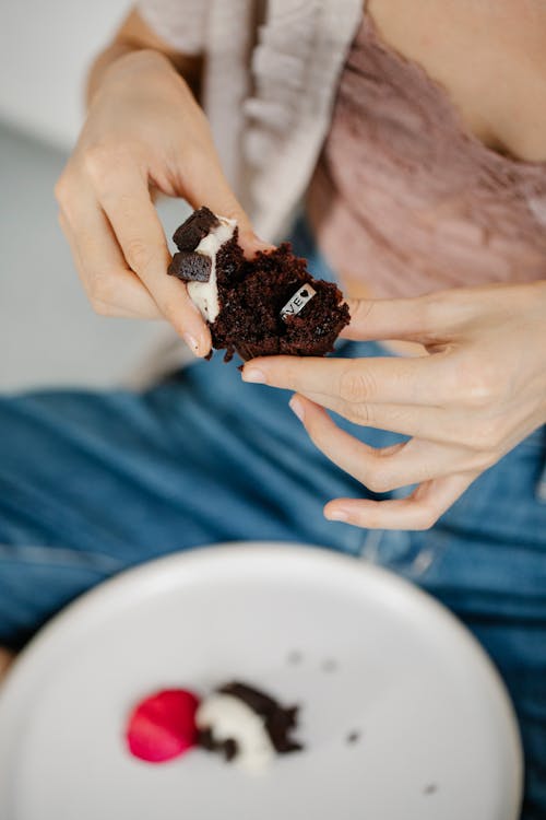Free From above of crop anonymous young stylish lady eating delicious sweet chocolate muffin with Love engraved silver ring inside on Saint Valentine Day Stock Photo