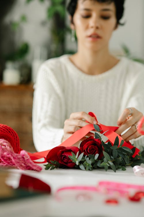 Young ethnic female florist tying bow on bunch of red roses